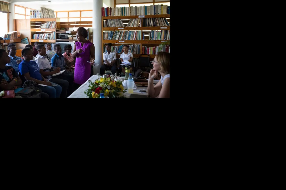 Au sein de la Commission nationale haïtienne de coopération avec l'Unesco (CNHCU), la MINUJUSTH a dévoilé les 33 fables produites pas des enfants dans le cadre de son concours #IlEtaitUneFABLE. Leonora Baumann / UN / MINUJUSTH, 2018 A group of people sitting in a library listening to a woman in a purple dress speaking to the group.