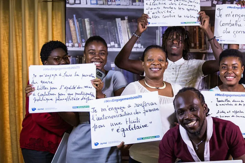 Des représentants des autorités et de la société civile haïtiennes participent à la campagne #MesEngagementsHAITI à l'occasion de la Journée internationale des Casques bleus des Nations Unies. Leonora Baumann / UN / MINUJUSTH, 2019 A group of people holding pieces of paper with wording on it smiling